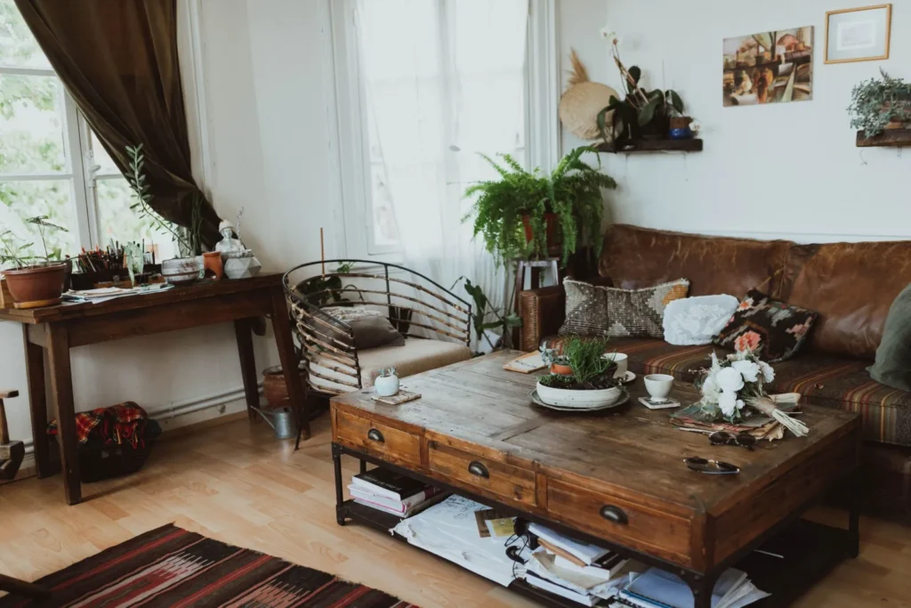 Small apartment living room mixing a leather sofa, rattan chair, and wood coffee table with patterned pillows and plants.